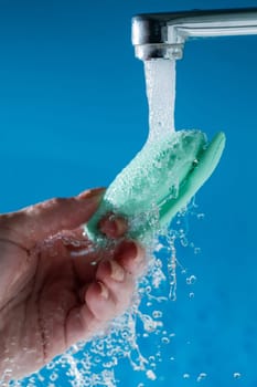 A woman washes a vibrator under running water on a blue background. Women's Health Kegel Trainer