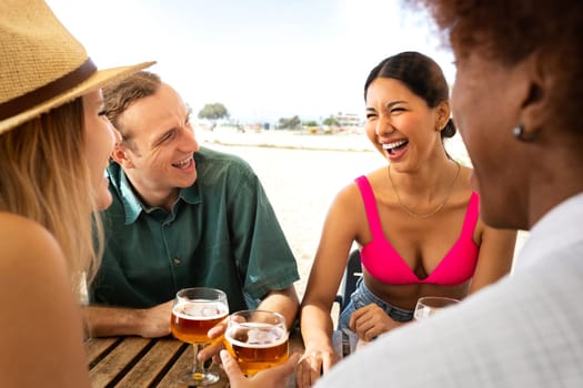 Young hispanic woman laughing and enjoying vacation with friends. Multiracial people having beer together at a beach bar. Lifestyle concept.