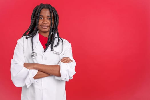 African female doctor smiling at the camera with arms crossed in studio with red background