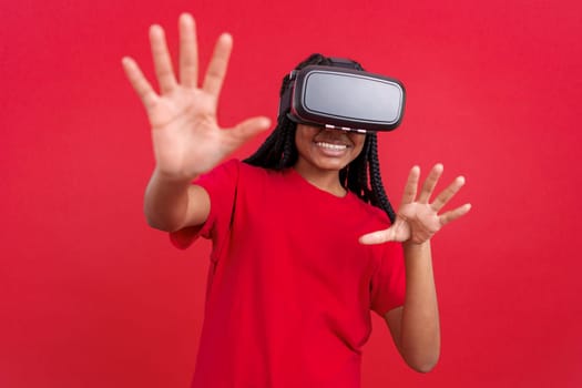 Happy african woman with Virtual Reality goggles in studio with red background
