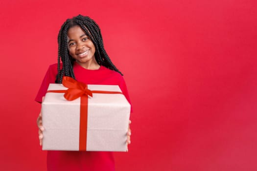 Happy african woman looking at the camera giving a present in studio with red background