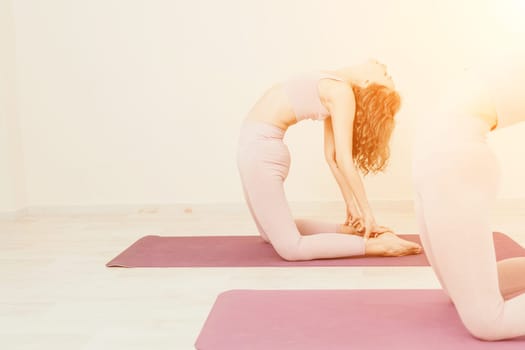 Young woman with long hair in white swimsuit and boho style braclets practicing outdoors on yoga mat by the sea on a sunset. Women's yoga fitness routine. Healthy lifestyle, harmony and meditation