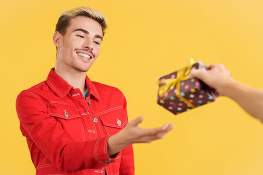 Gay man receiving a present from an unrecognizable person in studio with yellow background