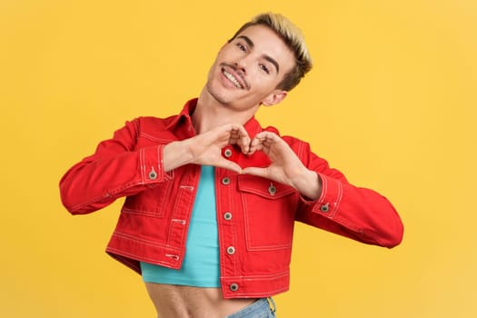 Gay man representing a heart in the shape with hands in studio with yellow background