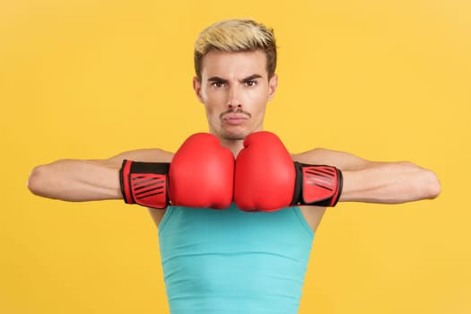 Gay man bumping his gloves looking at the camera seriously in studio with yellow background