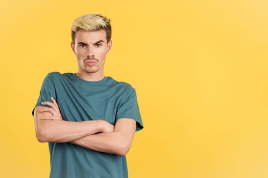 Gay man crossing the arms with an angry expression in studio with yellow background