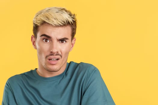 Gay man looking at the camera with a blank look on his face in studio with yellow background