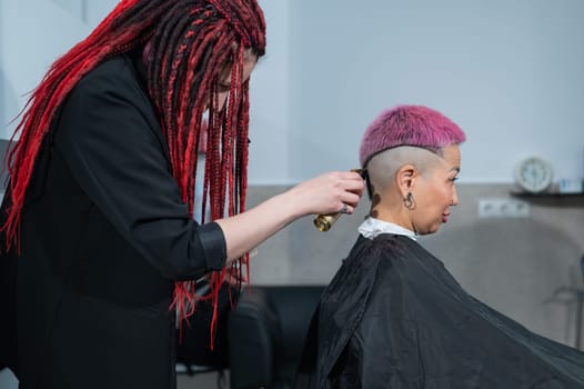 The hairdresser shaves the temple of a female client. Asian woman with short pink hair in barbershop