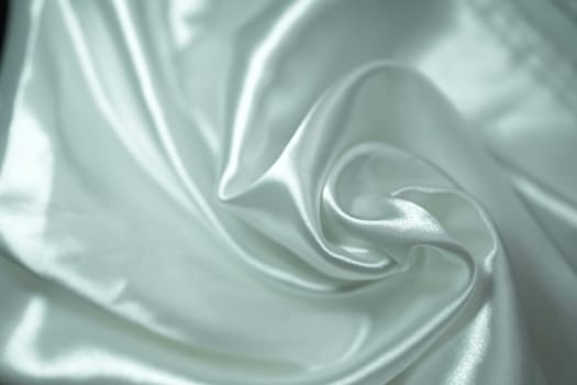 White satin fabric background with wavy soft folds for selling product. White Texture - light Wavy Glossy Silk Drapery. Shiny smooth fabric. Elegant background for design.