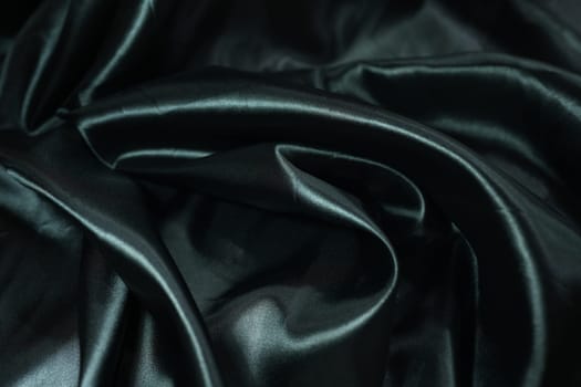 Black satin fabric background with wavy soft folds for selling product. Black Texture - Dark Wavy Glossy Silk Drapery. Black silk satin. Shiny smooth fabric. Elegant background for design.