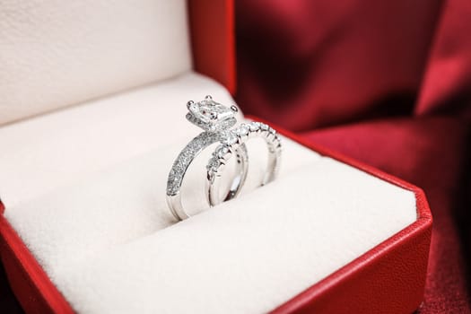 Luxury jewelryFine jewelry as diamond ring on white gold or platinum setting with red satin fabric background. Jewelry Luxury shop concept for engagement couple lover