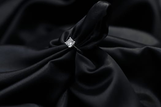 Fine jewelry as diamond ring in white gold or platinum setting with black satin fabric background. Jewelry shop concept for luxury store. engagement ring foe wedding couple lover