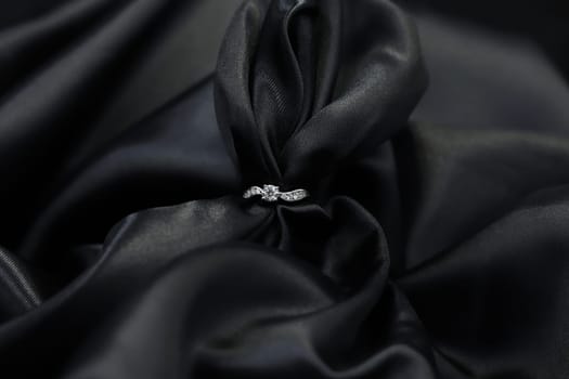 Fine jewelry as diamond ring in white gold or platinum setting with black satin fabric background. Jewelry shop concept for luxury store. engagement ring foe wedding couple lover