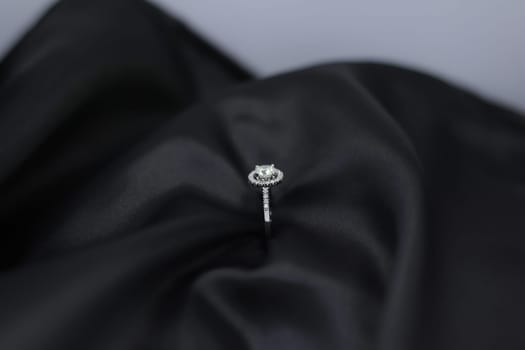 Fine jewelry as diamond ring in white gold or platinum setting with black satin fabric background. Jewelry shop concept for luxury store. engagement ring foe wedding couple lover