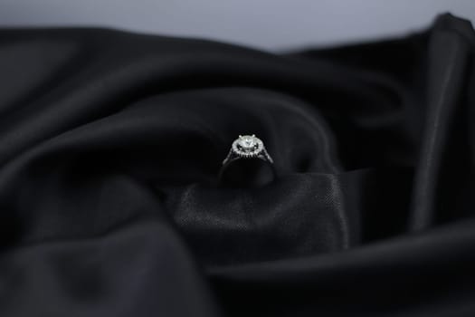 Fine jewelry as diamond ring in white gold or platinum setting with black satin fabric background. Jewelry shop concept for luxury store. engagement ring foe wedding couple lover