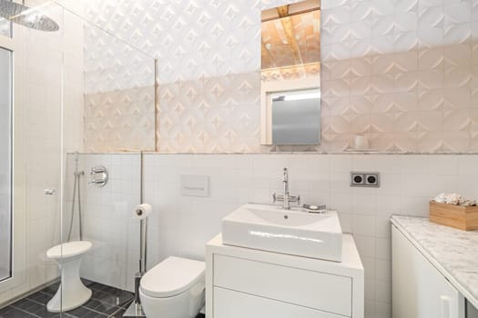 Modern refurbished tiled bathroom with shower zone, toilet, white sink and mirror