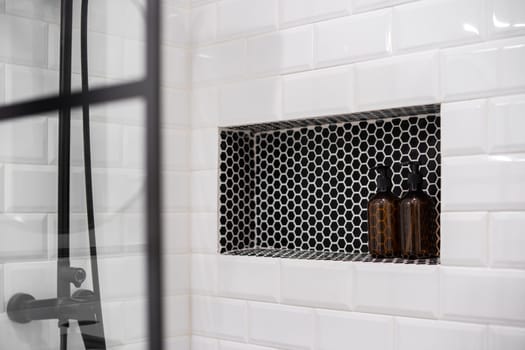 Built-in shelf with bottles in modern bathroom. Shower wall with white tiles