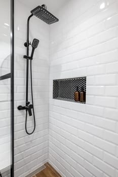 New black shower head on holder in white tiled bathroom in modern apartment