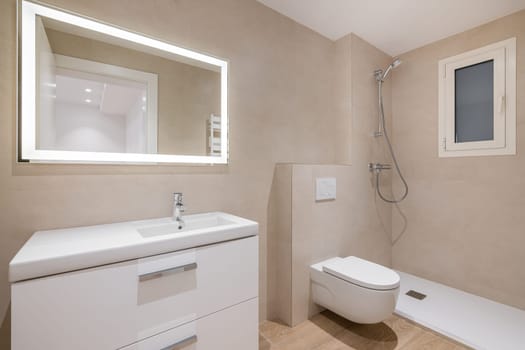 Modern bathroom with beige tiles, shower, toilet and rectangular large mirror with lighting.