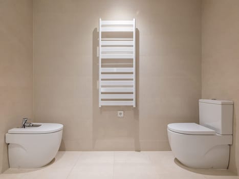 Toilet, bidet and heating radiator in a modern bathroom with beige tiles