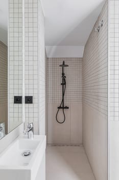 Narrow bathroom with shower zone and small sink. Interior of modern bathroom with beige tiles
