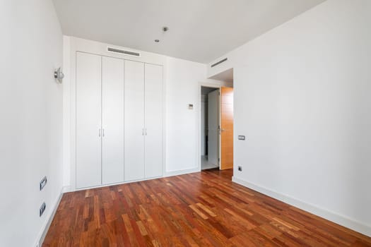 Interior of empty apartment, white room with built-in wardrobe and parquet floor.