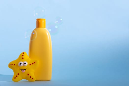 Yellow plastic bottle with baby cosmetic and funny bath toy. Soap bubbles on a background. The concept of children's bath time