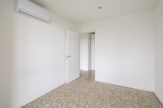 Interior of empty apartment, white room with air conditioning and tiled floor.