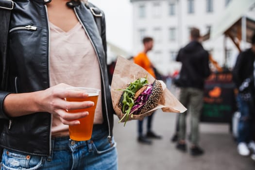 Close up of woman hands holding delicious organic salmon vegetarian burger and homebrewed IPA beer on open air beer an burger urban street food festival in Ljubljana, Slovenia