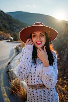 Woman road mountain. A woman in a white sweater, black boots and a hat walks along a winding alpine path between the mountains at sunset in late summer. The concept of travel