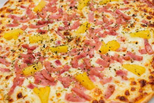 Hawaiian pizza. Close-up of pizza topped with pineapple, ham, cheese and oregano. Selective focus.
