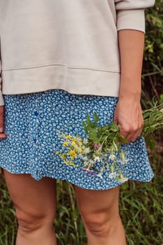 A girl in a blue skirt and a white blouse stands with wildflowers in her hand
