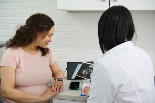 Smiling mature pregnant woman visits doctor gynecologist obstetrician in gynecological clinic, during regular medical checkup. Pregnancy and maternity concept. Healthcare and medicine. Ultrasonography