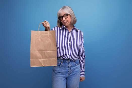 fashionable middle aged woman with gray hair holding social help package on bright studio background with copy space.