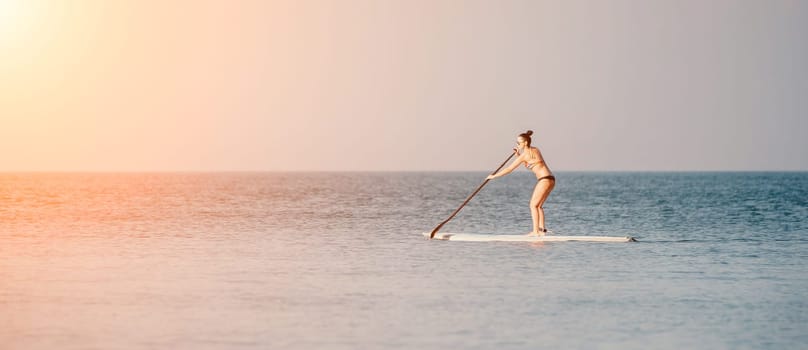 Sea woman sup. Silhouette of happy middle aged woman in rainbow bikini, surfing on SUP board, confident paddling through water surface. Idyllic sunset. Active lifestyle at sea or river