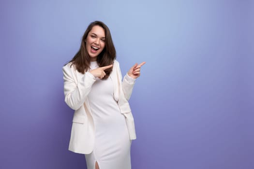 cheerful brunette woman in ivory jacket and white dress posing in studio.