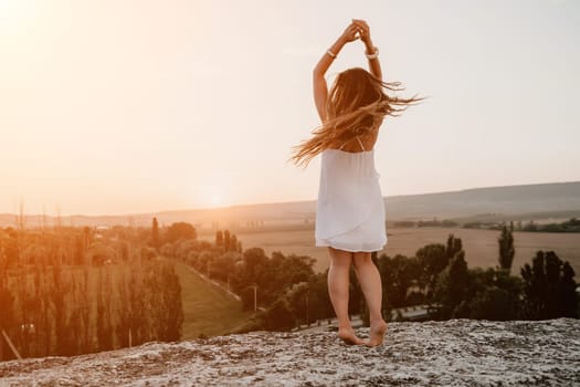 Romantic beautiful bride in white dress posing with sea and mountains in background. Stylish bride standing back on beautiful landscape of sea and mountains on sunset