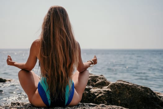 Woman sea yoga. Back view of free calm happy satisfied woman with long hair standing on top rock with yoga position against of sky by the sea. Healthy lifestyle outdoors in nature, fitness concept.