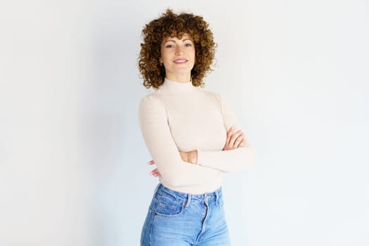 Positive adult female in casual apparel keeping arms crossed while standing against white background and looking at camera