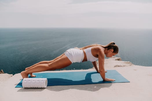 Middle aged well looking woman with black hair doing Pilates with the ring on the yoga mat near the sea on the pebble beach. Female fitness yoga concept. Healthy lifestyle, harmony and meditation.