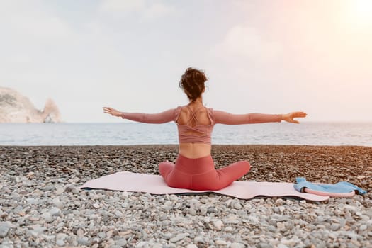 Middle aged well looking woman with black hair doing Pilates with the ring on the yoga mat near the sea on the pebble beach. Female fitness yoga concept. Healthy lifestyle, harmony and meditation.