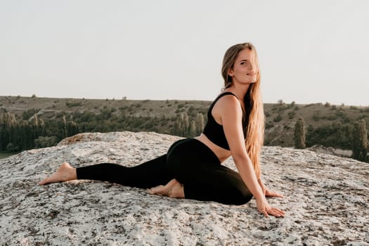 Well looking middle aged woman with long hair, fitness instructor in leggings and tops doing stretching and pilates on the rock near forest. Female fitness yoga routine concept. Healthy lifestyle.