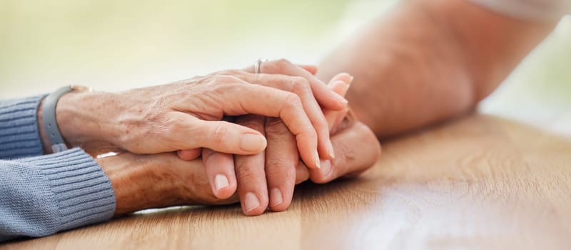 Senior, holding hands and support with couple, comfort and help on table for grief, pain or sympathy. Elderly man, old woman and helping hand for empathy, love and care in home with bonding together.