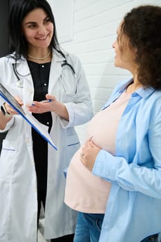 Confident experienced doctor gynecologist obstetrician holding clipboard with analyses and ultrasound scan results, explaining to pregnant woman the treatment that needs to perform in obstetric clinic