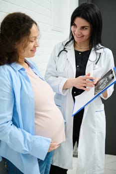 Multi-ethnic happy pregnant woman visiting gynecologist obstetrician doctor at maternity hospital or medical clinic for pregnancy consultation. Pregnancy screening. Gynecology. Healthcare and medicine