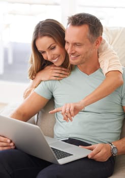 Happy couple, computer and pointing on home internet for online planning, website and to check application together. Hug, love and mature partner, woman or people on sofa reading on laptop technology.