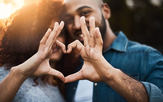 This is our love story. a a young couple making a heart shape with their fingers outdoors