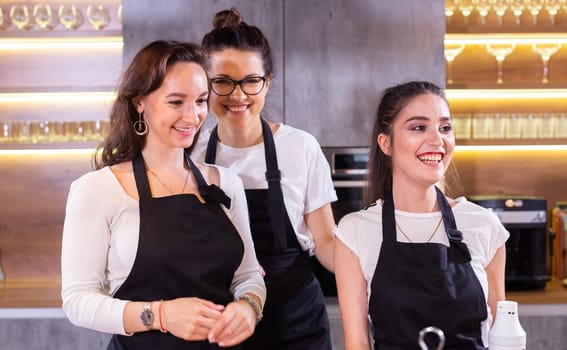 Three funny female chef in uniform holding cookies while smiling and having fun at camera in kitchen