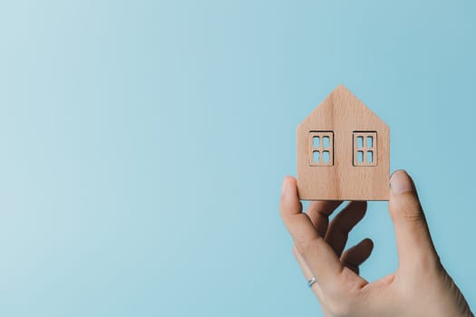 Hand holding a wooden house model on blue background for housing and property concept