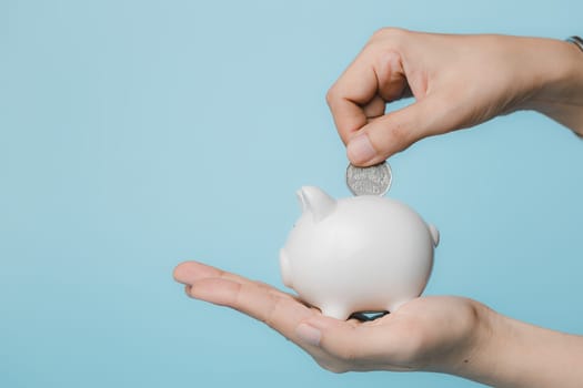 Hand saving a coin into piggy bank  on blue background for investment, business, finance and saving money concept.